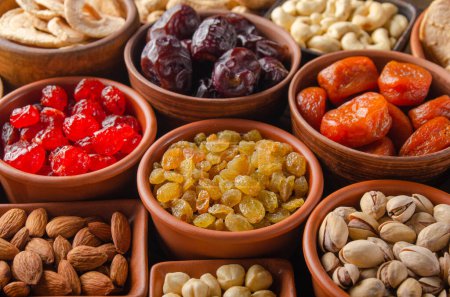 Different nuts and dried fruits in bowls on wooden kitchen table