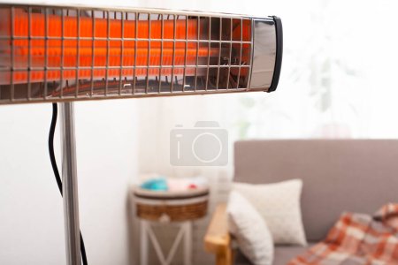 Calentador infrarrojo eléctrico que calienta la sala de estar con sofá y planta en maceta en el fondo
