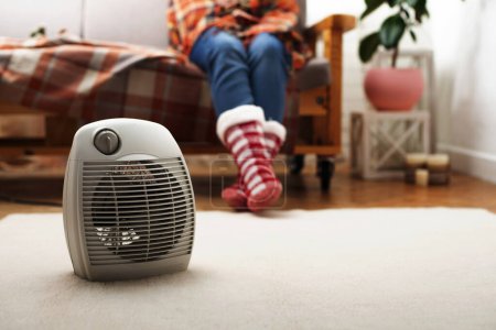 Calentador de ventilador eléctrico en el suelo en la sala de estar con humano sentado en el sofá en el fondo