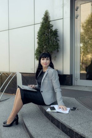 Foto de Mujer de negocios confiada en ropa casual y con una computadora portátil y un cuaderno en el fondo del centro de negocios. El concepto de trabajar en Internet - Imagen libre de derechos