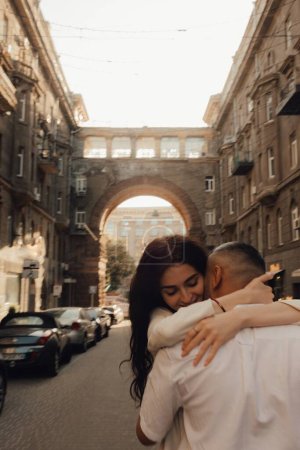 Photo for The couple walks around Kyiv. Old city. Love story. Walk around the city. A woman in a white suit. Guy in a t-shirt and jeans. Love and hugs. To cross the road. No focus blurred and noise effect. - Royalty Free Image