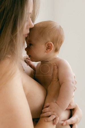 Photo for Nude woman with baby in her arms on lighte background. Happy motherhood and breastfeeding concept. Photos with soft focus. Good morning concept. Cute naked baby looking at the camera. - Royalty Free Image