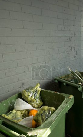 Foto de Latas de basura con brócoli y verduras podridas en envases de plástico cerca de una tienda de comestibles. - Imagen libre de derechos