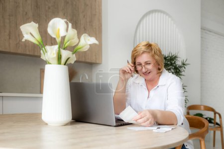 Ältere Geschäftsfrau mit Laptop in der Hand. Alte Dame verwaltet Kontofinanzierung, berechnet Geldhaushaltssteuer, plant Bankkredit Schulden Rentenzahlung sitzen zu Hause Küchentisch.