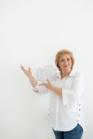 Photo for Smiling confident middle aged business woman points with hands to space for text on white background. Old senior businesswoman, 60s professional female manager, leader looking at camera, copy space. - Royalty Free Image