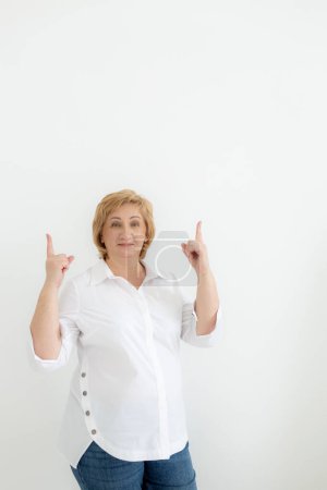 Photo for Smiling confident middle aged business woman points with hands to space for text on white background. Old senior businesswoman, 60s professional female manager, leader looking at camera, copy space. - Royalty Free Image