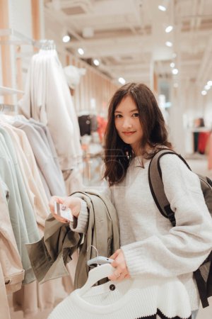 Photo for Korean teenage girl holds a credit card in her hands and wants to pay for new clothes in a shopping mall. Retail and consumerism. Sale promotion and shopping concept. Part of a series. - Royalty Free Image