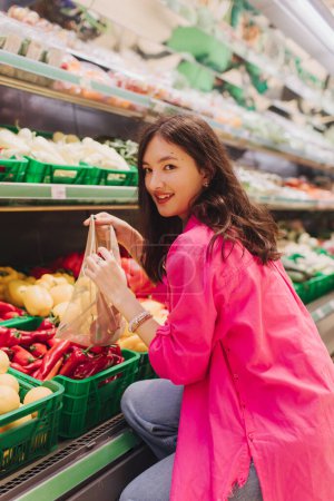 Foto de Mujer coreana joven comprando sin bolsas de plástico en la tienda de comestibles. Chica vegana de cero residuos eligiendo frutas y verduras frescas en el supermercado. Parte de una serie. - Imagen libre de derechos