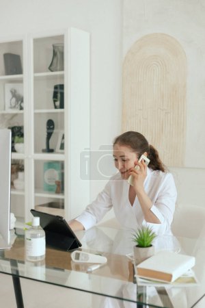 Medicine, healthcare and technology concept - Friendly female gp physician doctor in white uniform using software application on digital tablet, analyzing medical history in the clinic office.