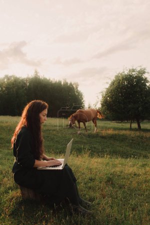 Foto de Mujer usando laptop en IT afuera en eco-granja. Charla en línea. Pase tiempo libre en la naturaleza. Concepto de trabajo desde casa, vida lenta, mantenerse conectado, distanciamiento social, internet. Parte de la serie. - Imagen libre de derechos