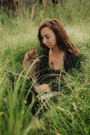 Mujer usando laptop en IT con gato afuera en eco-granja. Charla en línea. Pase tiempo libre en la naturaleza. Concepto de trabajo desde casa, vida lenta, mantenerse conectado, distanciamiento social, internet. Parte de la serie.