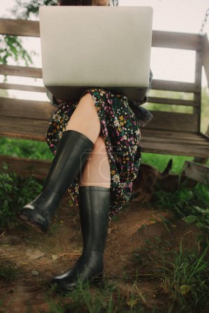 Photo for Close up female legs in rubber galoshes with laptop in IT outside in eco-farm. Spend free time on nature. Concept working from home, slow life, social distancing, internet. Part of the series. - Royalty Free Image