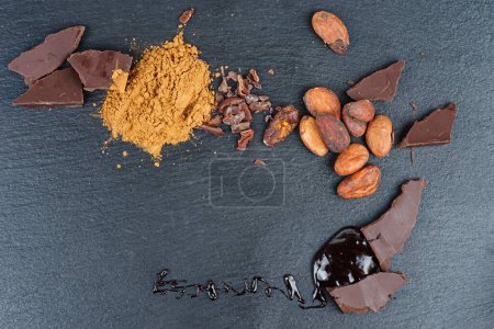 Foto de Chocolate negro casero, almendras, cacao (molido y frijoles) sobre fondo de pizarra de piedra negra - Imagen libre de derechos