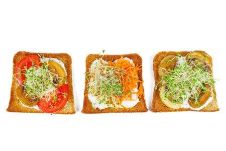 Foto de Brotes de alfalfa verde, tomates frescos y secos sobre rebanadas tostadas de pan integral aisladas sobre fondo blanco - Imagen libre de derechos