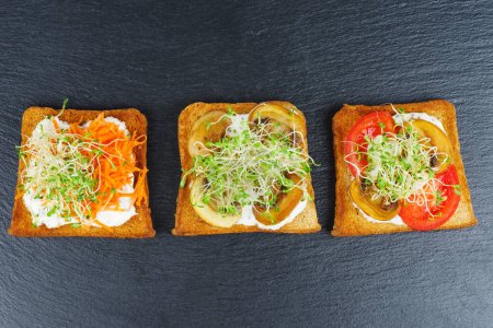 Photo for Green alfalfa sprouts,fresh and dried tomatoes on toasted slices of wholegrain bread isolated on black stone - Royalty Free Image