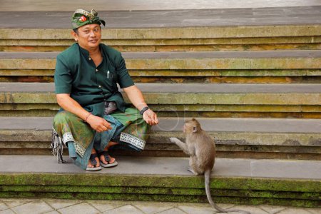 Téléchargez les photos : Ubud, Bali, Indonésie - 6 septembre : Un garde-singe officiel avec un petit singe dans la forêt sacrée du sanctuaire des singes - une attraction touristique populaire - en image libre de droit