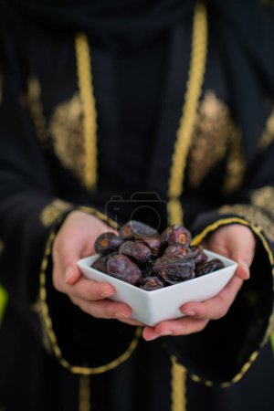 Foto de Mujer musulmana moderna sosteniendo un plato lleno de dátiles dulces en el tiempo iftar en Ramadán Kareem concepto de comida saludable islámica fondo verde OVNI. Foto de alta calidad - Imagen libre de derechos