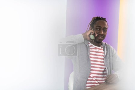 Photo for Smiling young african man freelancer using laptop and smartphone studying online working from home. - Royalty Free Image