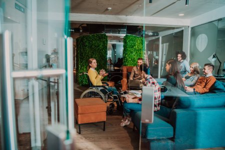 Eine Geschäftsfrau im Rollstuhl bei einem Geschäftstreffen mit dem Team in einem modernen Büro. Eine Gruppe junger Freiberufler einigt sich auf neue Online-Business-Projekte. 