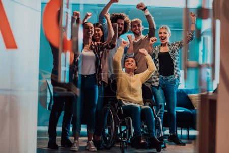 Photo of business women in wheelchairs with their hands raised in the air with their colleagues, together celebrating business success. 