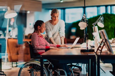 Businesswoman in a wheelchair working in a creative office. Business team in modern coworking office space. Colleagues working in the background at late night. High quality photo