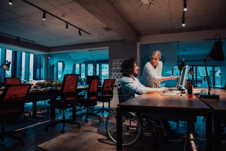 Photo for A businessman in a wheelchair in a modern coworking office space working with a female colleague late at nigh. Colleagues in the background. High quality photo - Royalty Free Image
