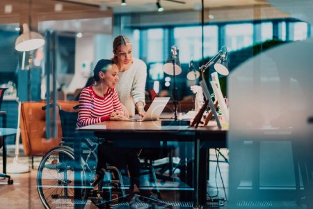 Photo for Businesswoman in a wheelchair working in a creative office. Business team in modern coworking office space. Colleagues working in the background at late night. High quality photo - Royalty Free Image