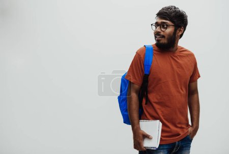 Foto de Estudiante indio con una mochila azul, gafas y cuaderno posando sobre fondo gris. El concepto de educación y escolarización. Hora de volver a la escuela. - Imagen libre de derechos