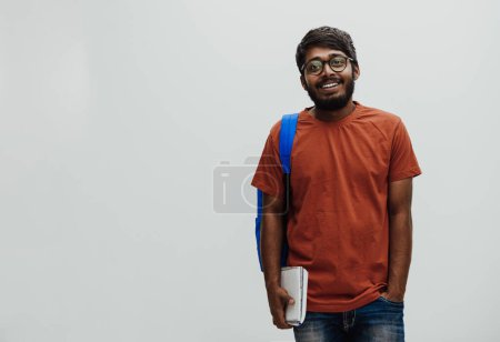  Indischer Student mit blauem Rucksack, Brille und Notizbuch posiert auf grauem Hintergrund. Das Bildungs- und Schulkonzept. Zeit, wieder zur Schule zu gehen. 