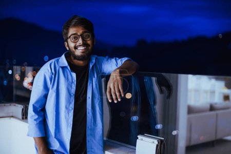 Photo for An Indian man with glasses and a blue shirt looks around the city at night. In the background of the night street of the city. High quality photo - Royalty Free Image