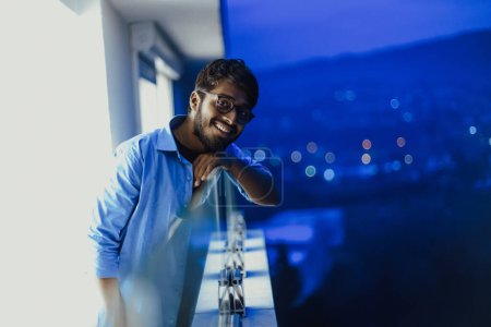 Photo for An Indian man with glasses and a blue shirt looks around the city at night. In the background of the night street of the city. High quality photo - Royalty Free Image