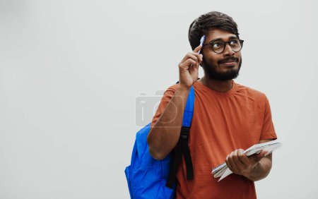 Foto de Estudiante indio confundido con una mochila azul, gafas y cuaderno posando sobre fondo gris. El concepto de educación y escolarización. Hora de volver a la escuela. - Imagen libre de derechos