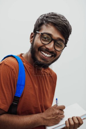 Foto de Estudiante indio con una mochila azul, gafas y cuaderno posando sobre fondo gris. El concepto de educación y escolarización. Hora de volver a la escuela. - Imagen libre de derechos