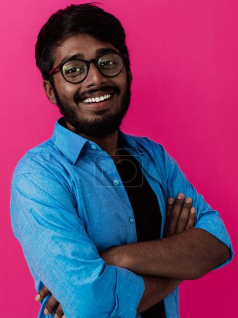 Foto de Hombre joven sonriente indio con camisa azul y gafas posando sobre fondo rosa. - Imagen libre de derechos