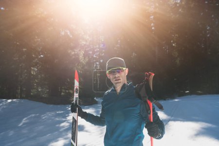 Foto de Retrato apuesto atleta masculino con esquís de fondo en las manos y gafas, entrenamiento en el bosque nevado. Concepto saludable de estilo de vida invernal. Foto de alta calidad - Imagen libre de derechos