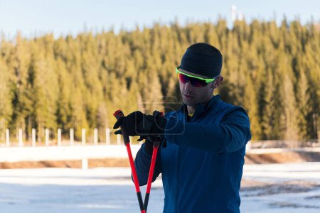 Téléchargez les photos : Athlète masculin séduisant avec des skis de fond, respirant fraîchement et faisant une pause après un entraînement difficile dans une forêt enneigée. Je vérifie les montres intelligentes. Mode de vie sain en hiver. Photo de haute qualité - en image libre de droit
