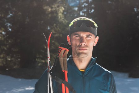 Foto de Retrato apuesto atleta masculino con esquís de fondo en las manos y gafas, entrenamiento en el bosque nevado. Concepto saludable de estilo de vida invernal. Foto de alta calidad - Imagen libre de derechos