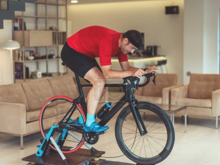 Téléchargez les photos : Un homme en vélo de triathlon sur une simulation de machine dans un salon moderne. Formation en cas de pandémie - en image libre de droit