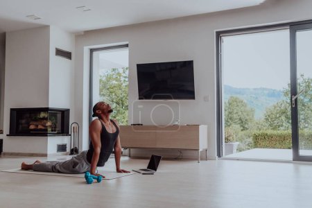 Téléchargez les photos : Entraînement à domicile. Homme sportif faisant la formation tout en regardant un tutoriel en ligne sur un ordinateur portable, l'exercice dans le salon, l'espace libre. - en image libre de droit