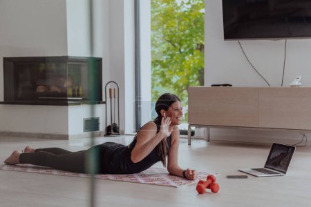 Téléchargez les photos : Jeune belle femme faisant de l'exercice, de l'étirement et pratiquant le yoga avec un entraîneur par vidéoconférence dans l'appartement lumineux Sunny Loft. Mode de vie sain, bien-être et pleine conscience Concept - en image libre de droit