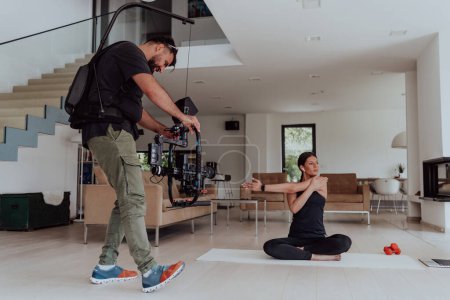 Téléchargez les photos : Dans les coulisses. Photo d'un caméraman enregistrant une femme faisant des exercices de yoga lors d'une formation en ligne tout en utilisant et en regardant un ordinateur portable. - en image libre de droit