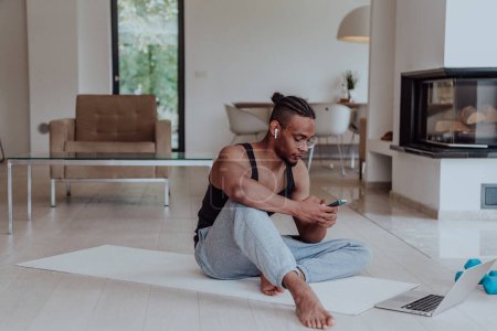 Photo for Training At Home. Sporty man doing training while watching online tutorial on laptop and using smartphone exercising in living room, free space - Royalty Free Image