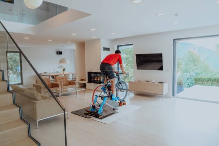 Foto de Un hombre montando una bicicleta de triatlón en una simulación de máquina en una sala de estar moderna. Entrenamiento en condiciones pandémicas - Imagen libre de derechos