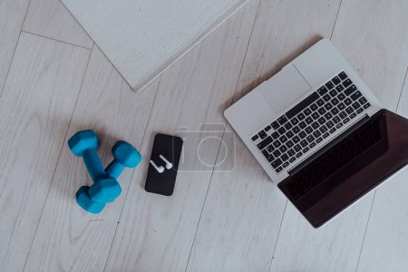 Foto de Foto de un ordenador portátil, mancuernas y auriculares en el suelo de la sala de estar. Concepto de formación en línea. Foto de alta calidad - Imagen libre de derechos