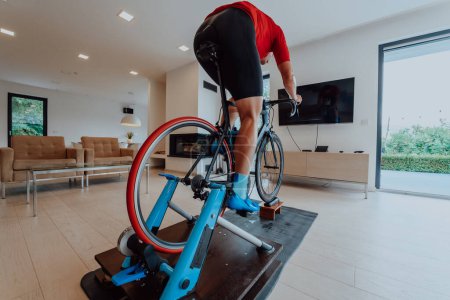 Photo for A man riding a triathlon bike on a machine simulation in a modern living room. Training during pandemic conditions - Royalty Free Image