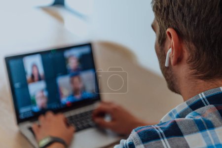 Photo for The man sitting at a table in a modern living room, with headphones using a laptop for business video chat, conversation with friends and entertainment. - Royalty Free Image