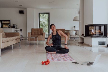 Téléchargez les photos : Jeune belle femme faisant de l'exercice, de l'étirement et pratiquant le yoga avec un entraîneur par vidéoconférence dans une maison ensoleillée lumineuse. Mode de vie sain, bien-être et pleine conscience Concept. - en image libre de droit