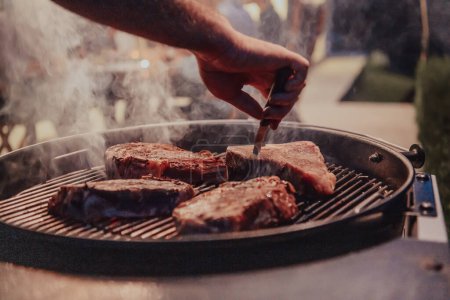 Photo for Close-up photo of delicious meat being grilled. In the background, friends and family are sitting and waiting for a meal. - Royalty Free Image