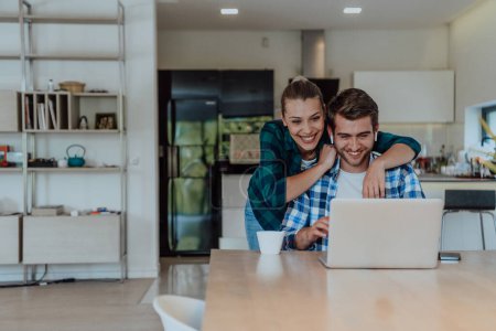 Photo for A young married couple is talking to parents, family and friends on a video call via a laptop while sitting in the living room of their modern house. - Royalty Free Image