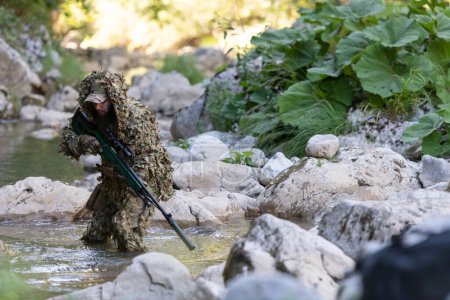 Photo for A military man or airsoft player in a camouflage suit sneaking the river and aims from a sniper rifle to the side or to target - Royalty Free Image